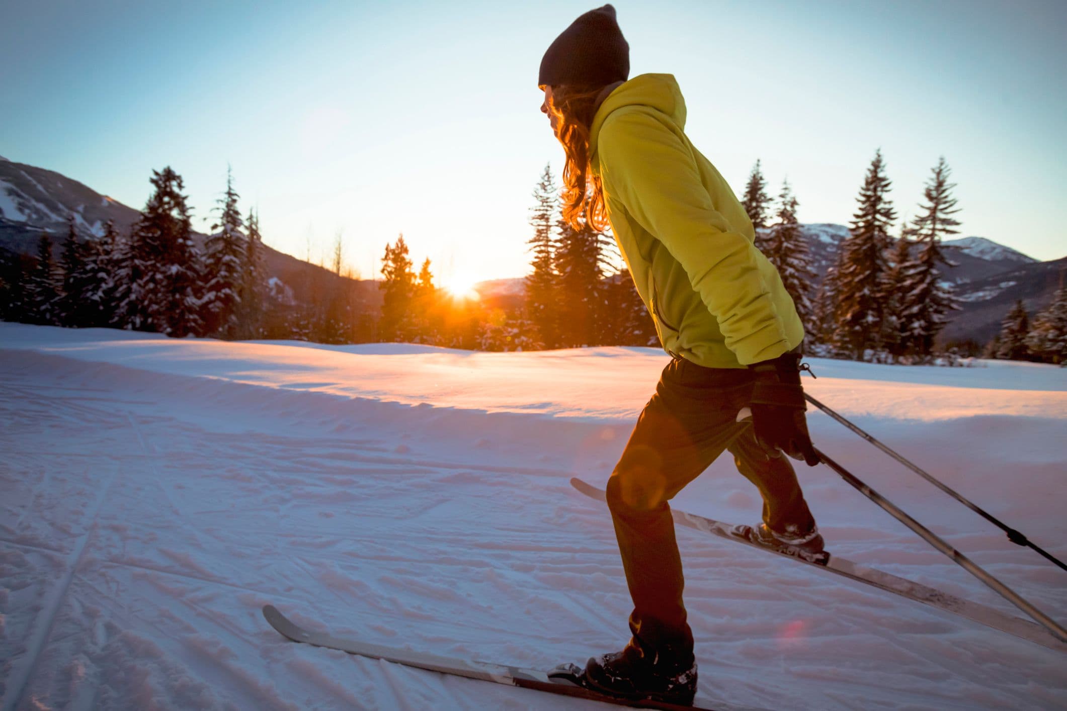 A woman cross country skiing while the sun is rising in the background.